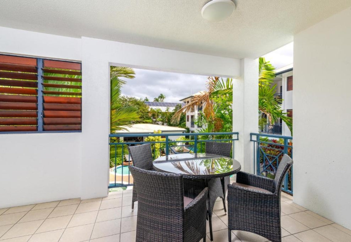 Balcony with a round glass table and four chairs, overlooking a pool and tropical garden at the Meridian Port Douglas Resort accommodation