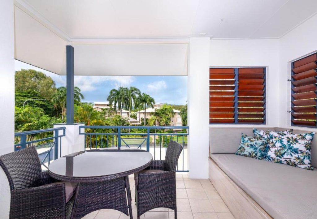 Outdoor patio area with table, chairs, and a bench with floral cushions, overlooking greenery at Meridian Port Douglas Resort.