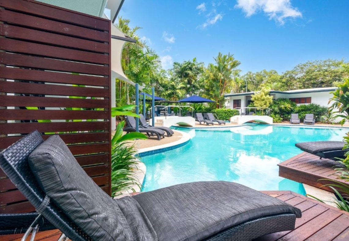 Pool area with lounge chairs, umbrellas, and a wooden deck at Meridian Port Douglas Resort