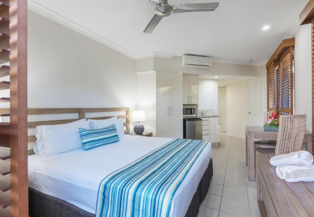 Bedroom with a bed, desk, and kitchen area in a studio hotel room at Meridian Port Douglas Resort.