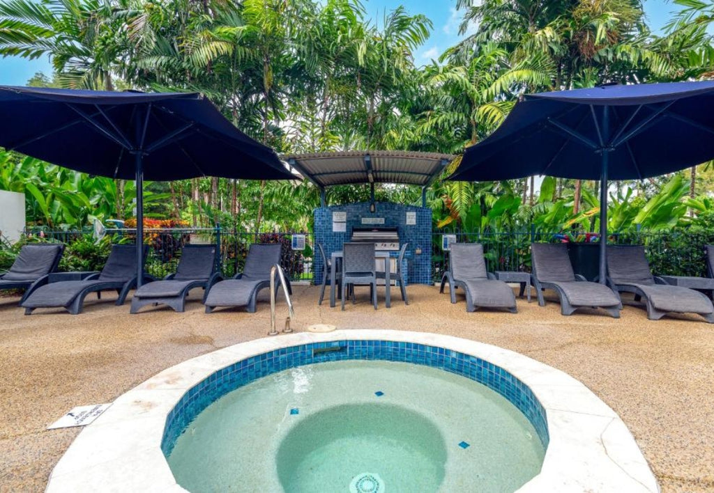 Resort BBQ area with outdoor setting with a hot tub, lounge chairs, and umbrellas surrounded by greenery at Meridian Port Douglas Resort