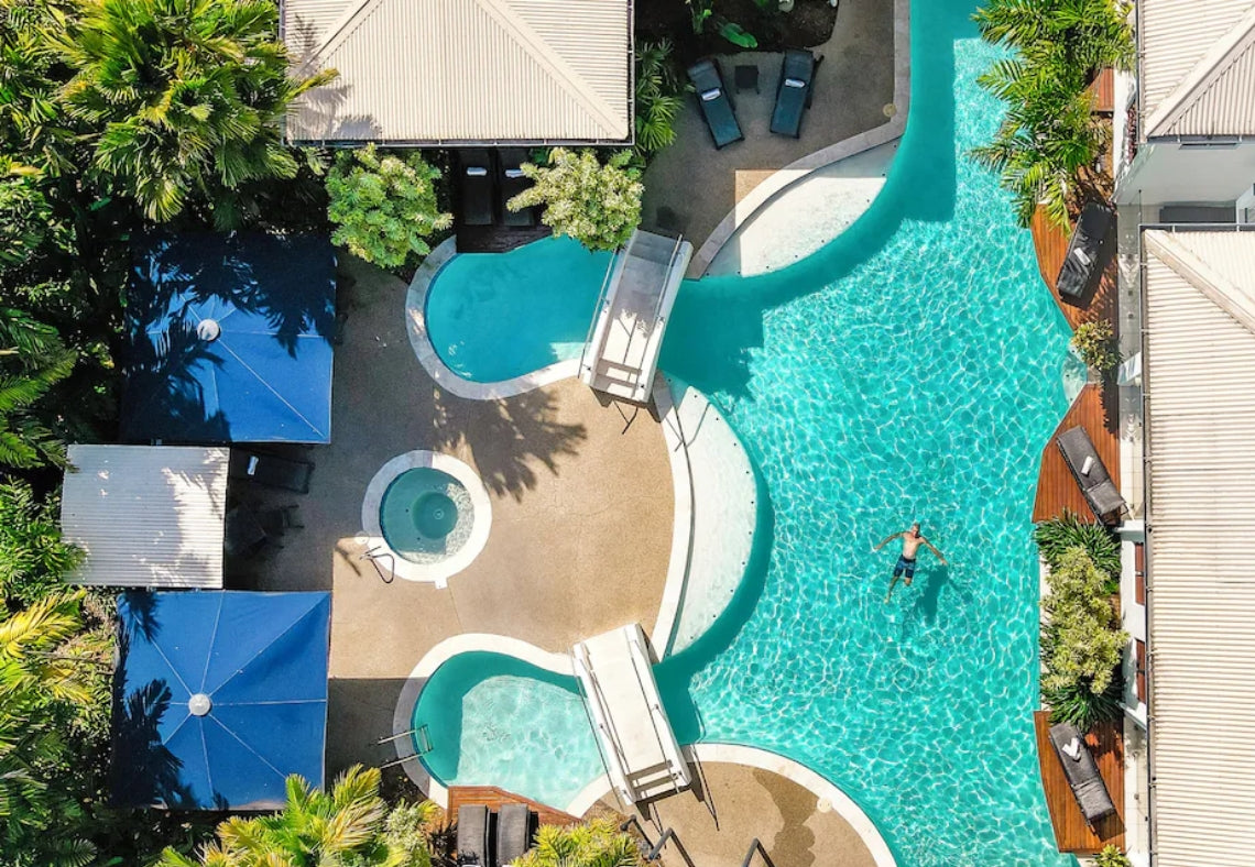 Aerial view of Meridian Port Douglas Resort swimming pool with lounge chairs and umbrellas surrounded by greenery.
