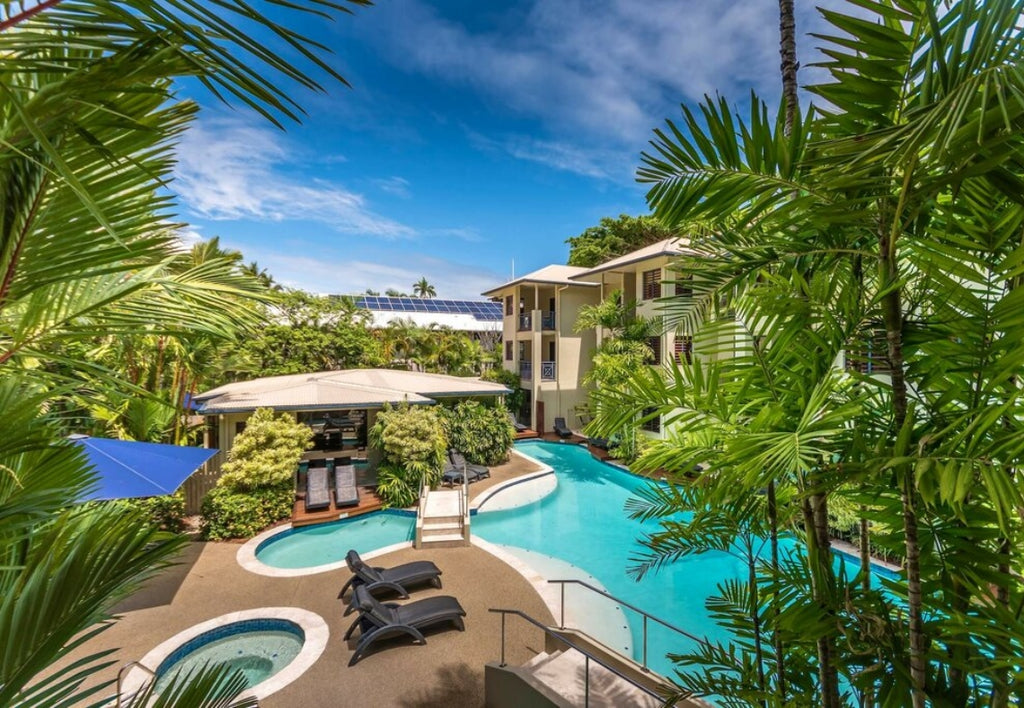 Meridian Resort Port Douglas Pool area with lounge chairs, palm trees, and a building in the background