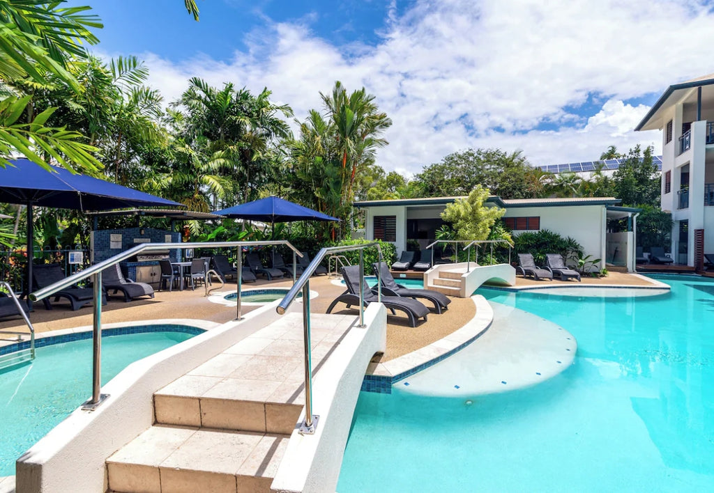 Meridian Resort Port Douglas Pool area with lounge chairs, umbrellas, and a building in the background