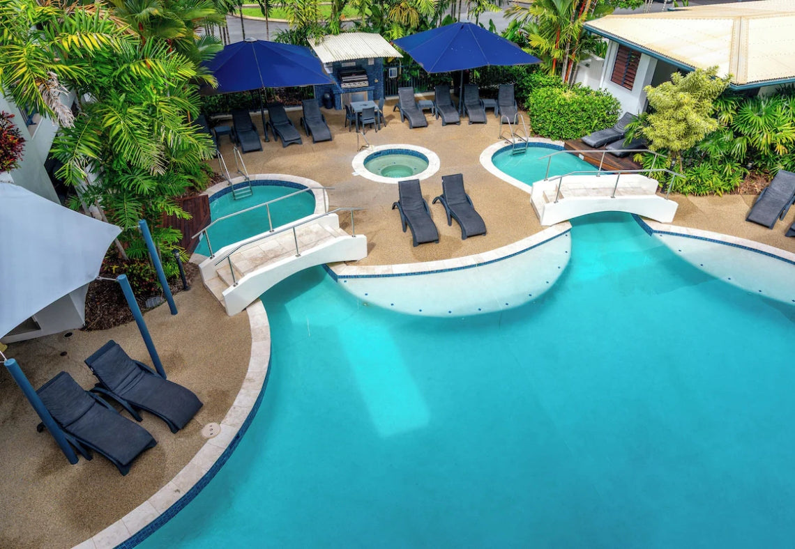 Meridian Port Douglas Resort Pool area with lounge chairs, umbrellas, and hot tub surrounded by greenery.
